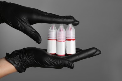 Professional cosmetologist holding bottles of pigments for permanent makeup on grey background, closeup