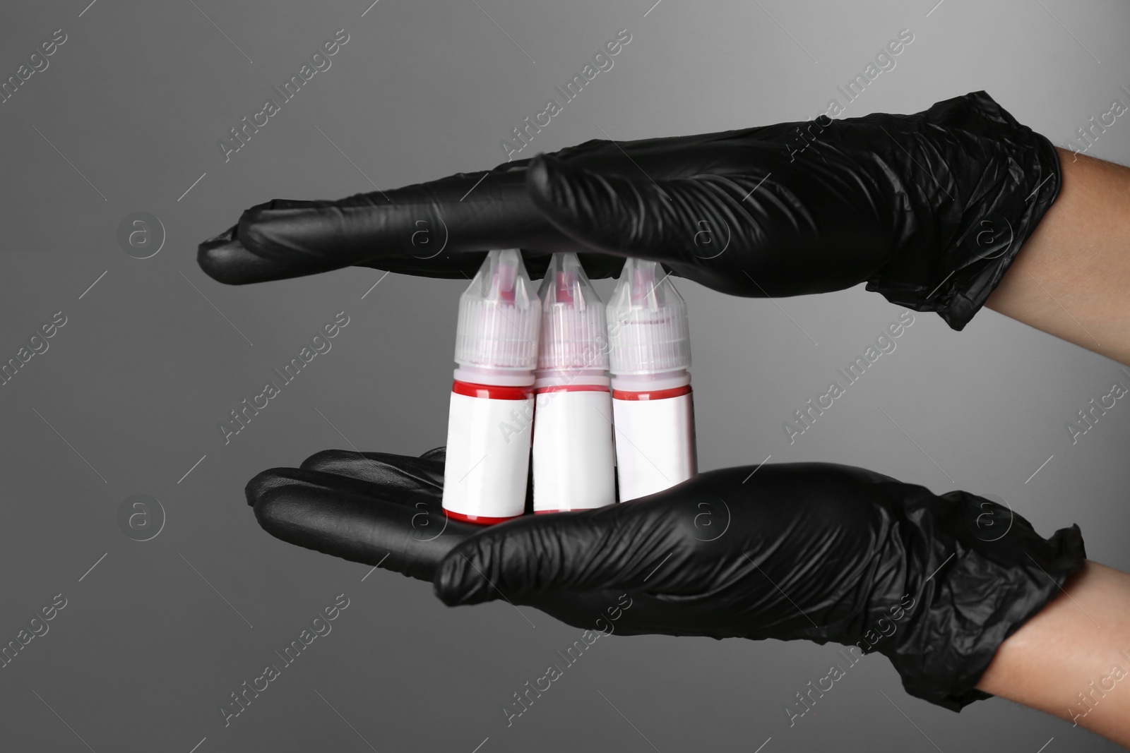 Photo of Professional cosmetologist holding bottles of pigments for permanent makeup on grey background, closeup