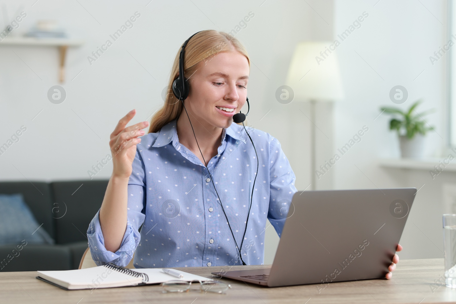 Photo of Interpreter in headset having video chat via laptop at table indoors