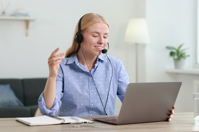 Photo of Interpreter in headset having video chat via laptop at table indoors