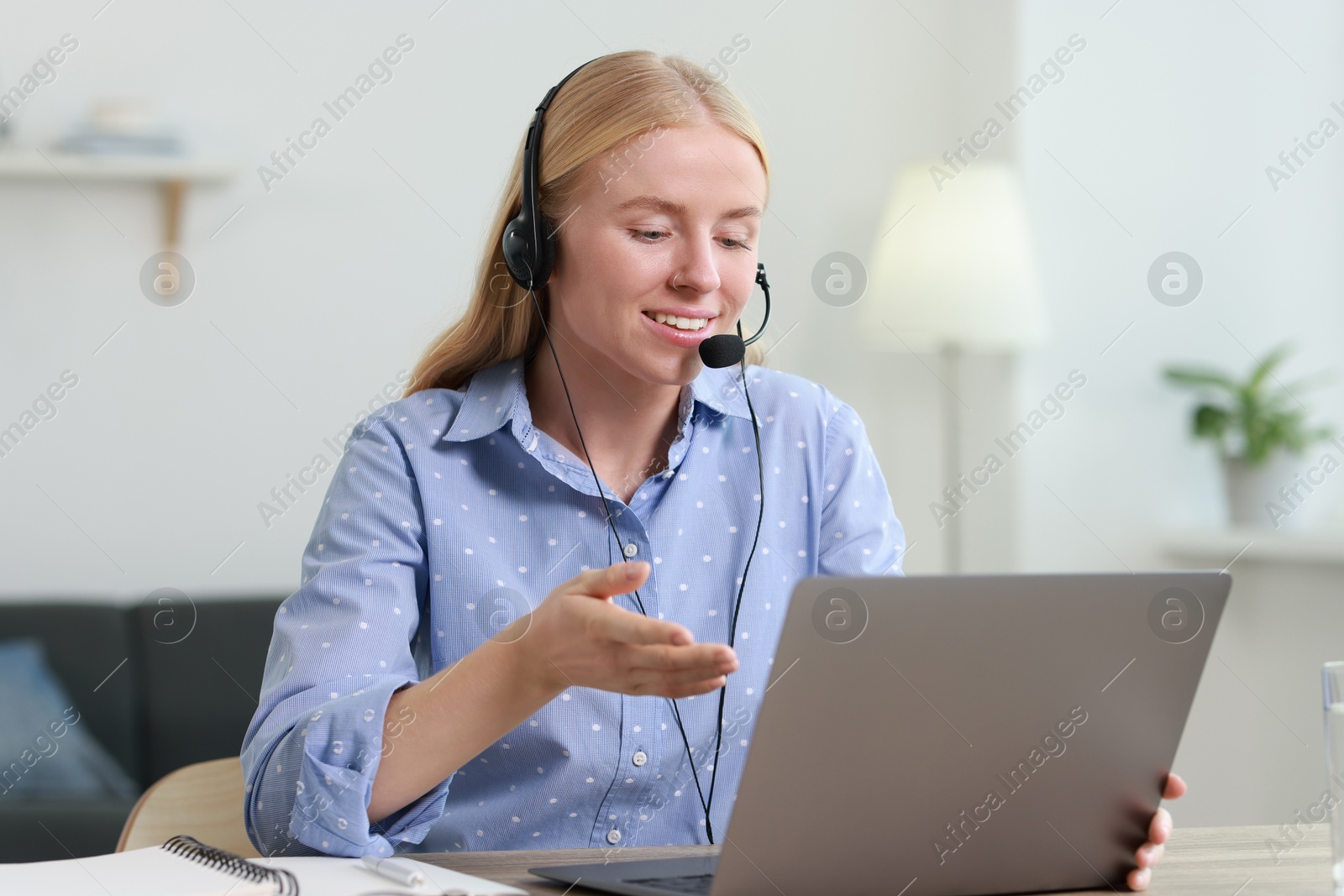 Photo of Interpreter in headset having video chat via laptop at table indoors