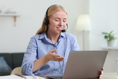 Photo of Interpreter in headset having video chat via laptop at table indoors