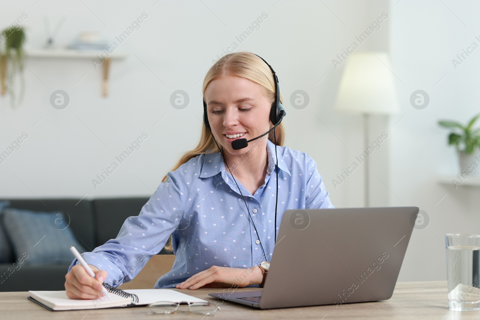 Photo of Interpreter in headset taking notes while working with laptop at table indoors