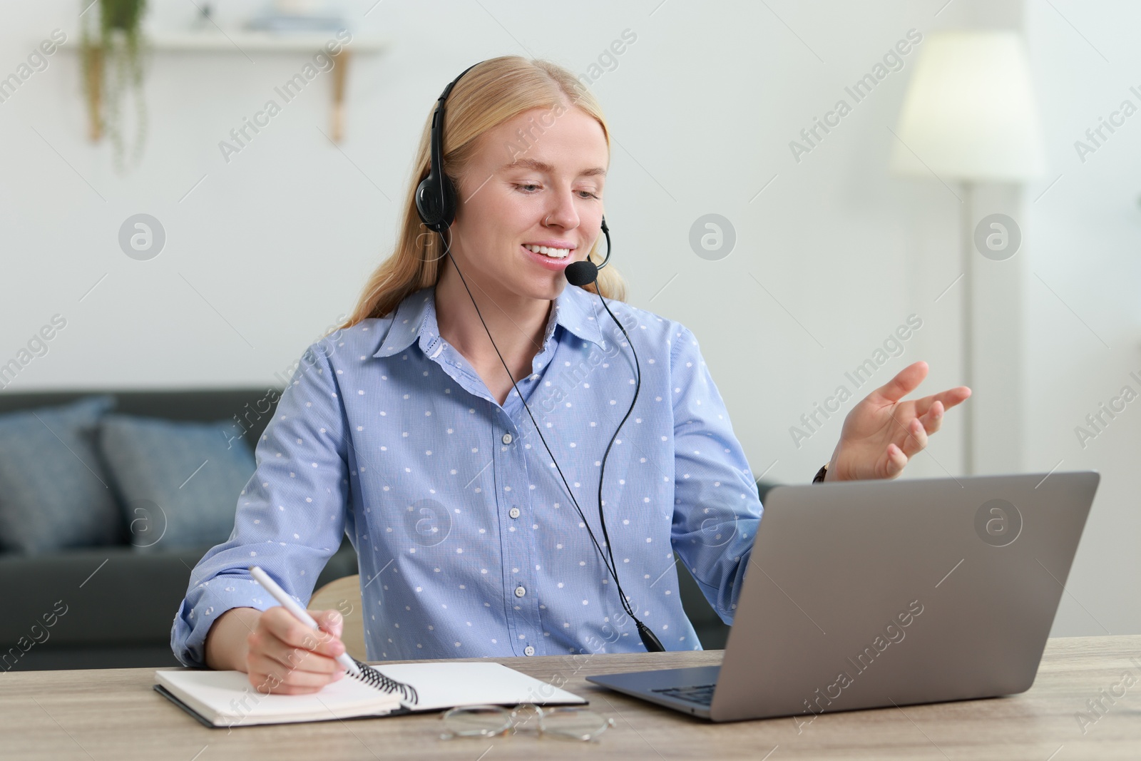 Photo of Interpreter in headset taking notes while working with laptop at table indoors