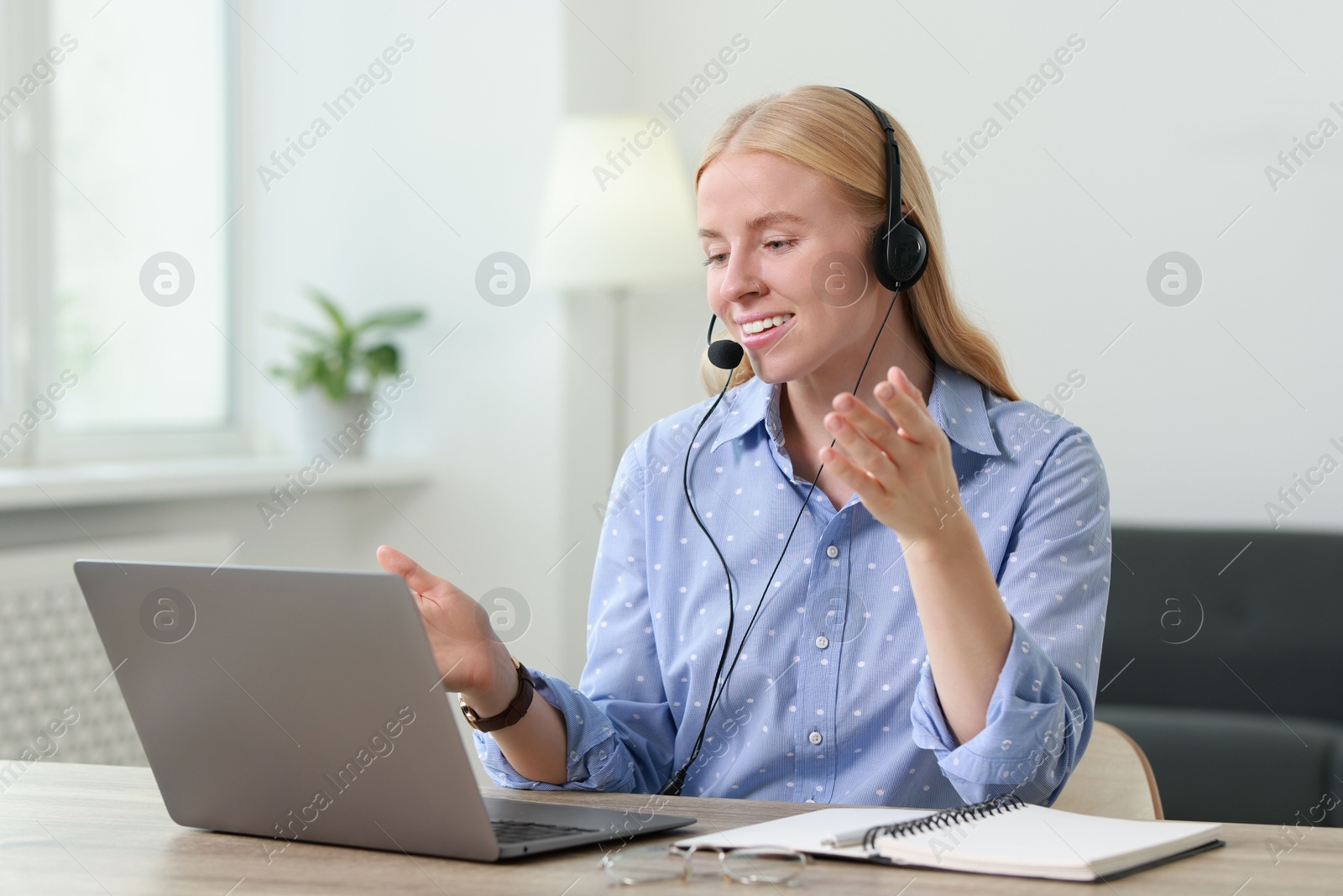 Photo of Interpreter in headset having video chat via laptop at table indoors