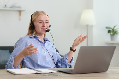 Photo of Interpreter in headset having video chat via laptop at table indoors