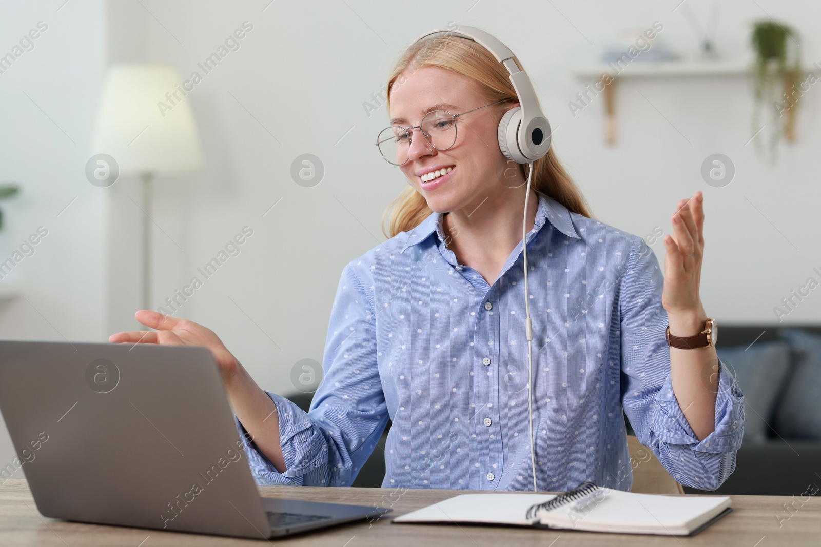 Photo of Interpreter in headphones having video chat via laptop at table indoors