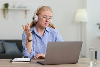 Interpreter in headphones having video chat via laptop at table indoors