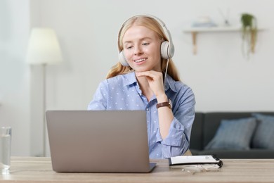 Interpreter in headphones working with laptop at table indoors