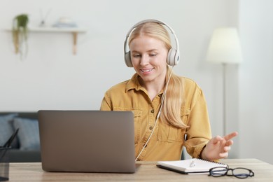 Photo of Interpreter in headphones working with laptop at table indoors