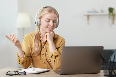 Interpreter in headphones having video chat via laptop at table indoors