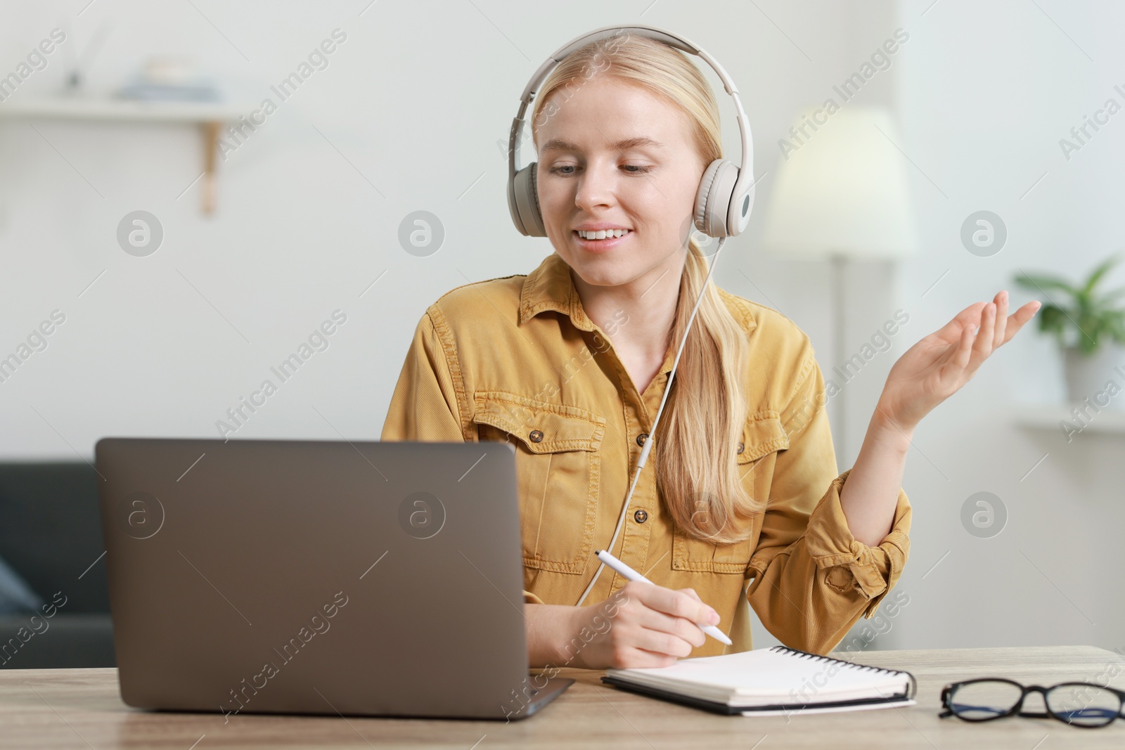 Photo of Interpreter in headphones taking notes while having video chat via laptop at table indoors