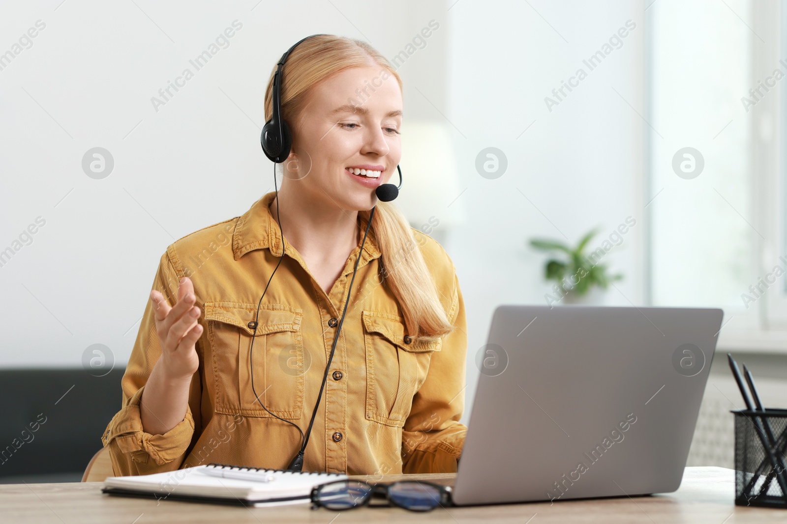 Photo of Interpreter in headset having video chat via laptop at table indoors