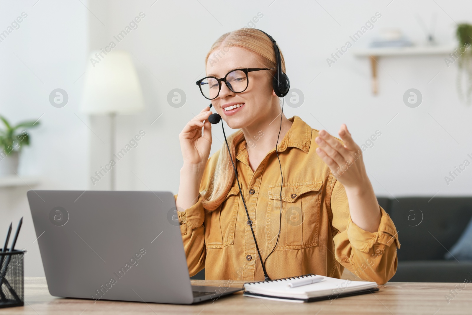 Photo of Interpreter in headset having video chat via laptop at table indoors