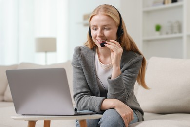 Photo of Interpreter in headset having video chat via laptop on sofa at home