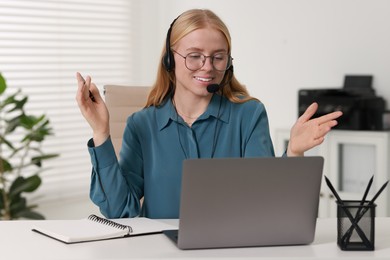 Interpreter in headset having video chat via laptop at table indoors