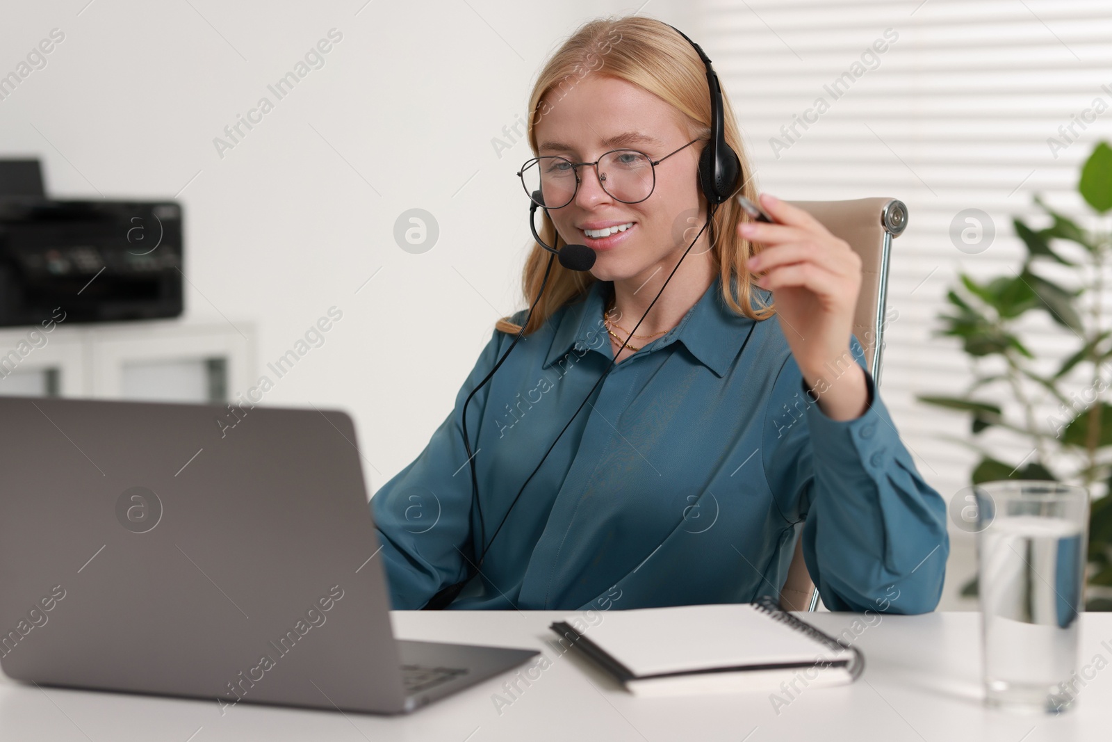 Photo of Interpreter in headset having video chat via laptop at table indoors