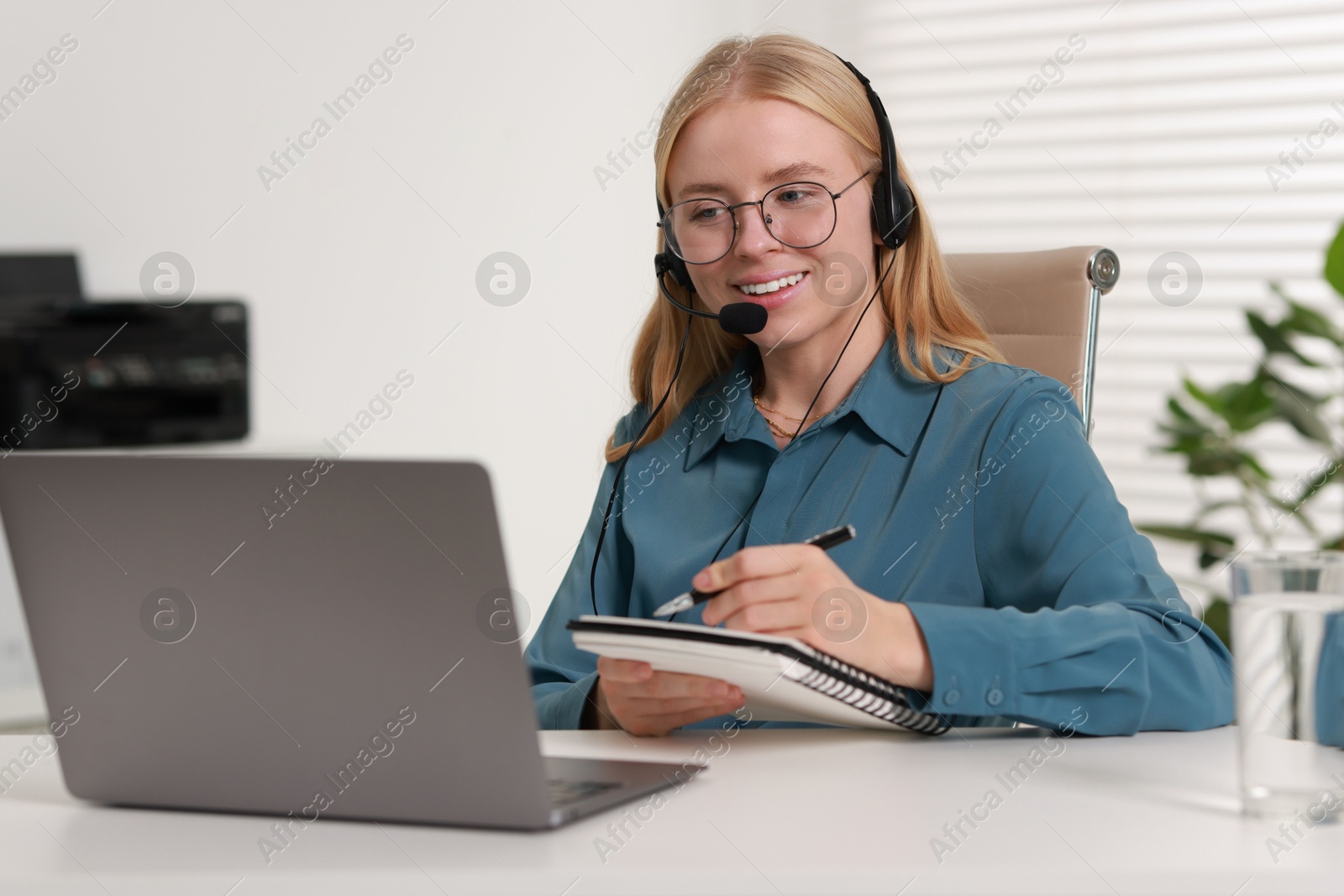 Photo of Interpreter in headset taking notes while working with laptop at table indoors