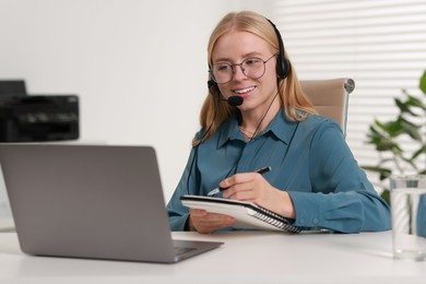 Interpreter in headset taking notes while working with laptop at table indoors