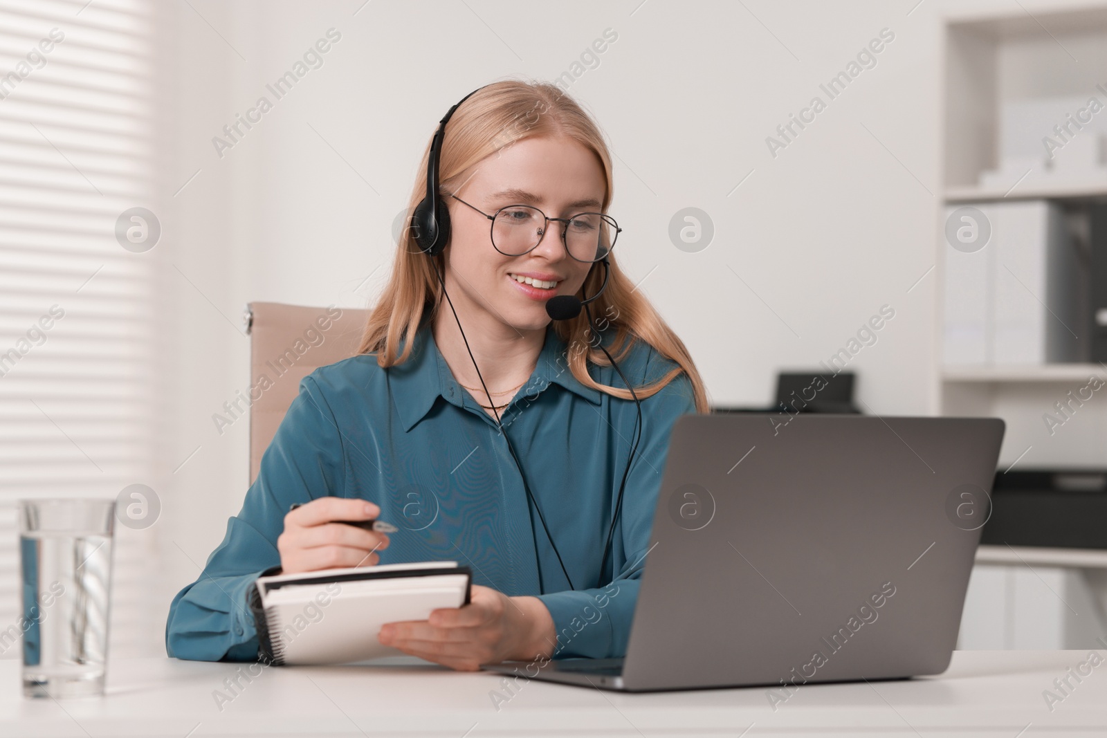 Photo of Interpreter in headset taking notes while working with laptop at table indoors