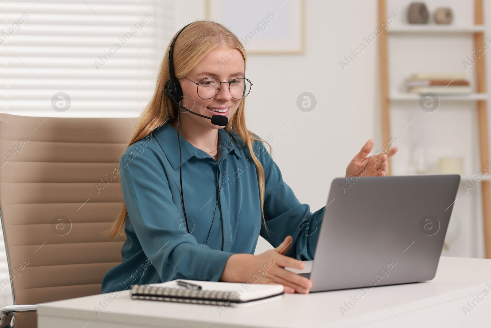 Photo of Interpreter in headset having video chat via laptop at table indoors