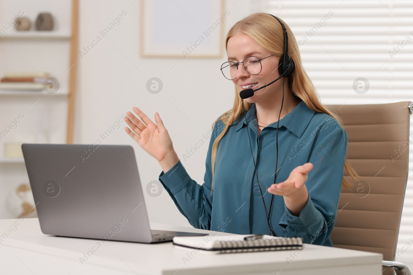 Photo of Interpreter in headset having video chat via laptop at table indoors