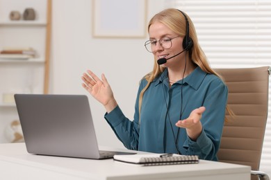 Interpreter in headset having video chat via laptop at table indoors