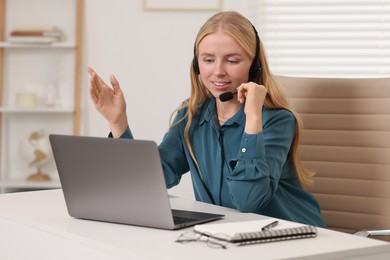 Interpreter in headset having video chat via laptop at table indoors