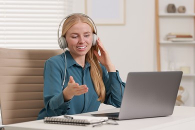 Interpreter in headphones having video chat via laptop at table indoors