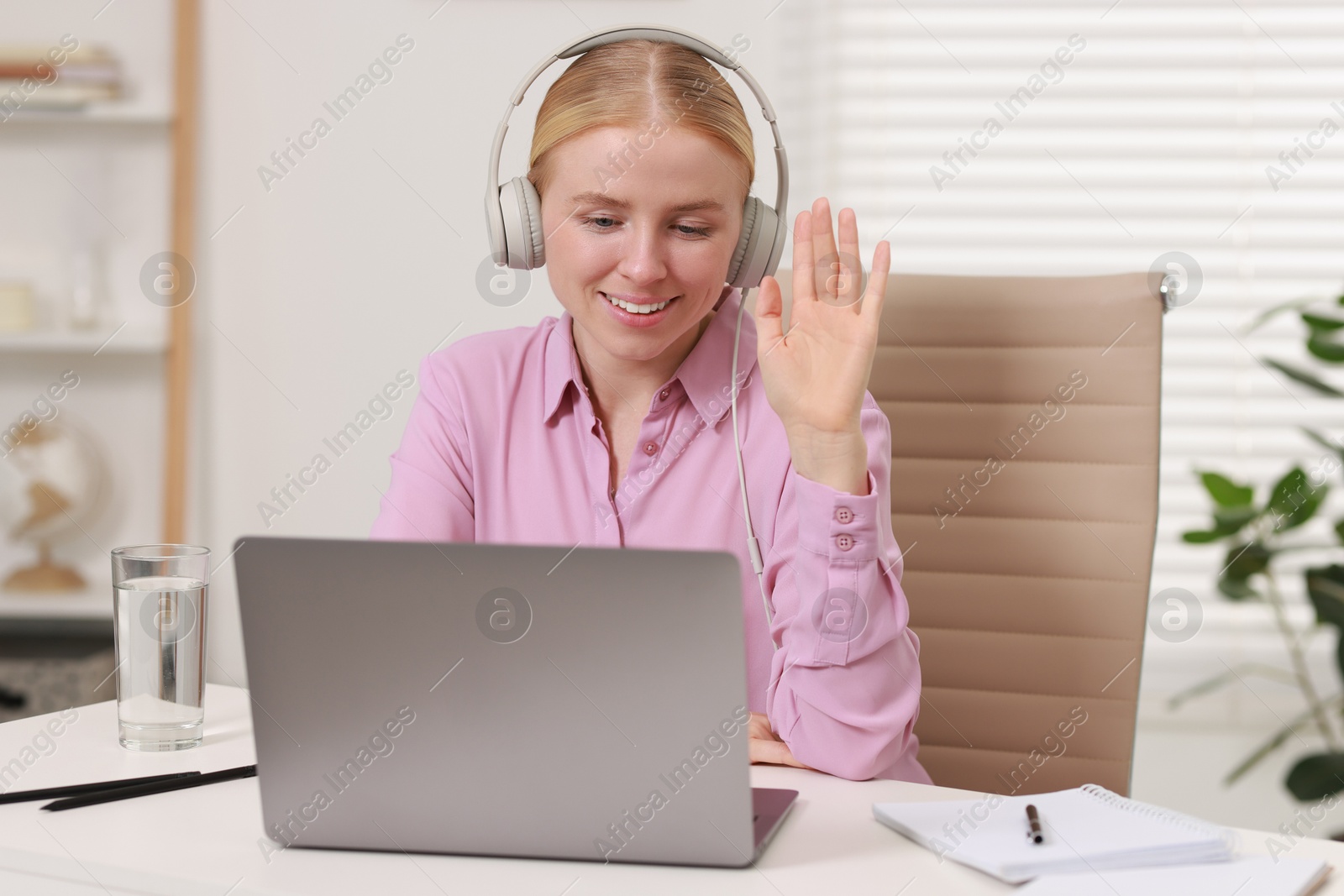 Photo of Interpreter in headphones having video chat via laptop at table indoors