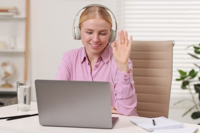 Interpreter in headphones having video chat via laptop at table indoors