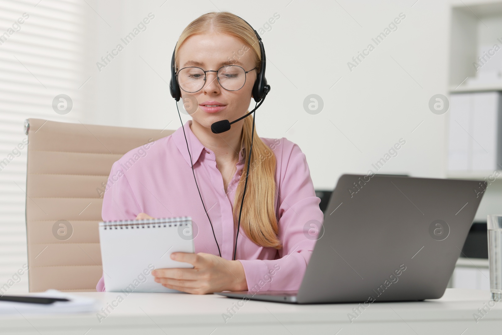 Photo of Interpreter in headset taking notes while working with laptop at table indoors