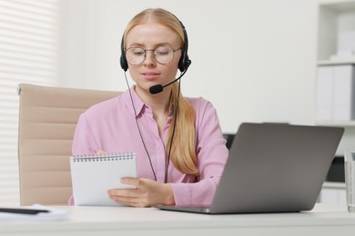 Photo of Interpreter in headset taking notes while working with laptop at table indoors