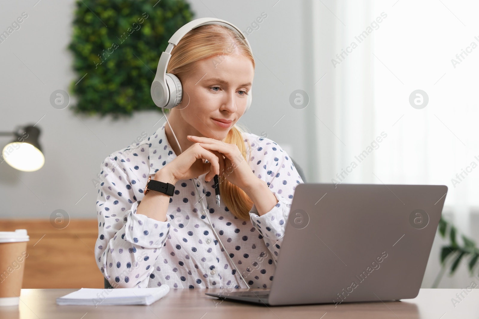 Photo of Interpreter in headphones working with laptop at table indoors