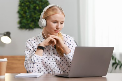 Photo of Interpreter in headphones working with laptop at table indoors