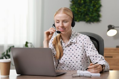 Photo of Interpreter in headset taking notes while working with laptop at table indoors