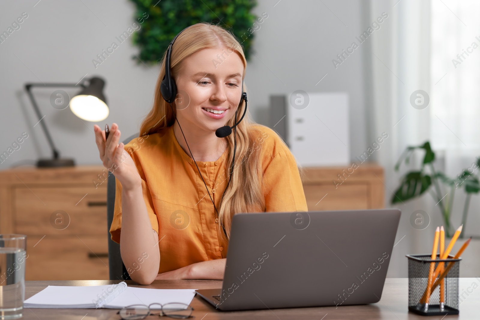 Photo of Interpreter in headset having video chat via laptop at table indoors