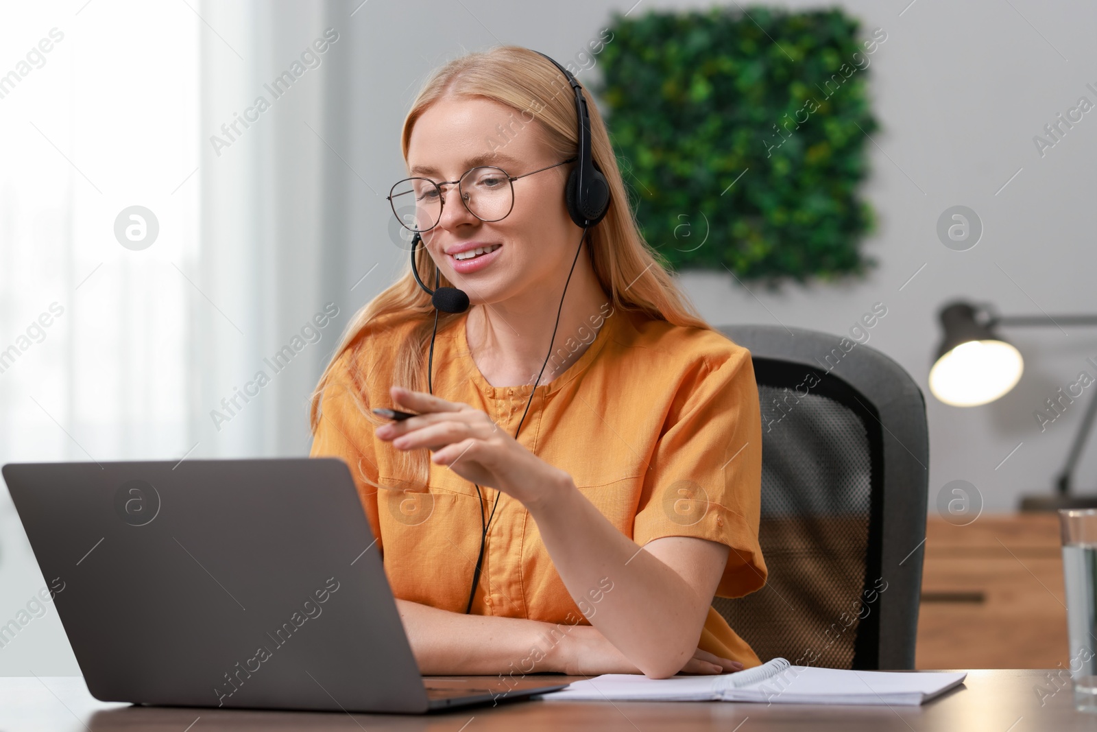 Photo of Interpreter in headset having video chat via laptop at table indoors