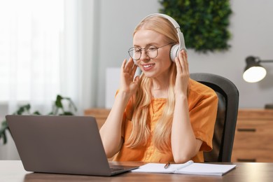 Interpreter in headphones working with laptop at table indoors