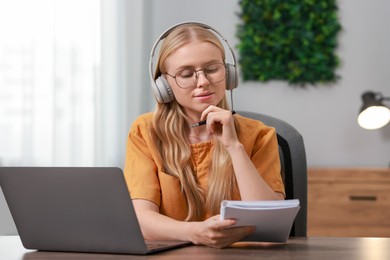 Photo of Interpreter in headphones working with laptop at table indoors