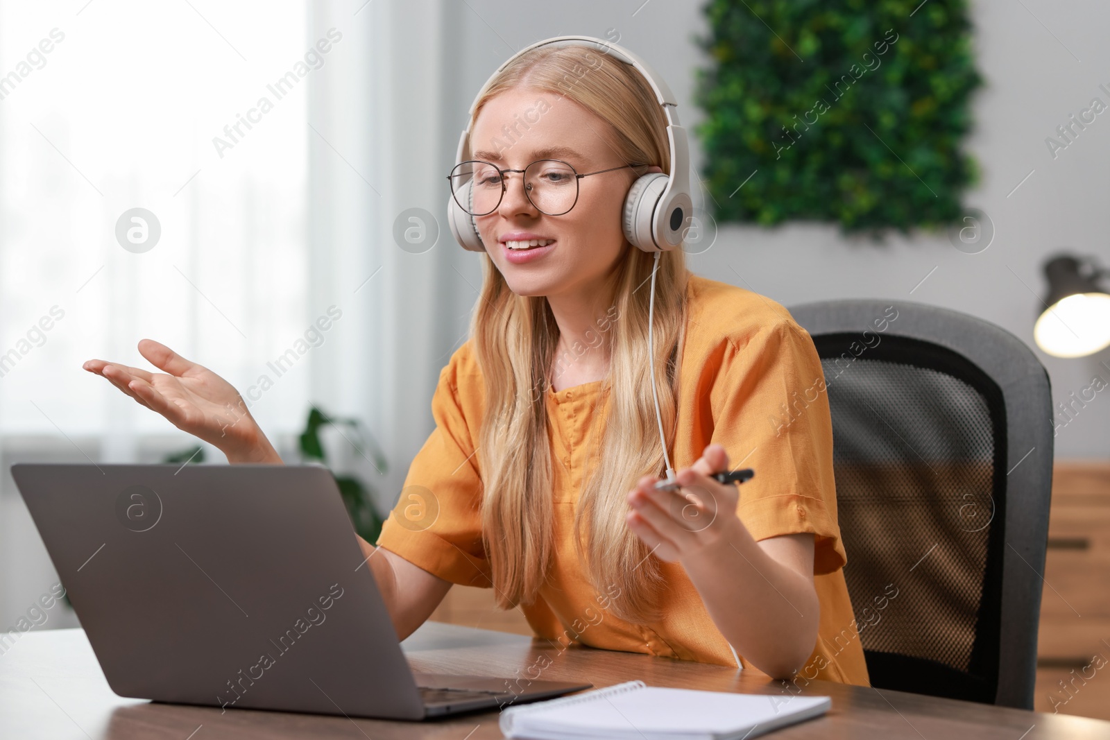 Photo of Interpreter in headphones having video chat via laptop at table indoors