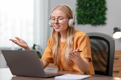 Photo of Interpreter in headphones having video chat via laptop at table indoors