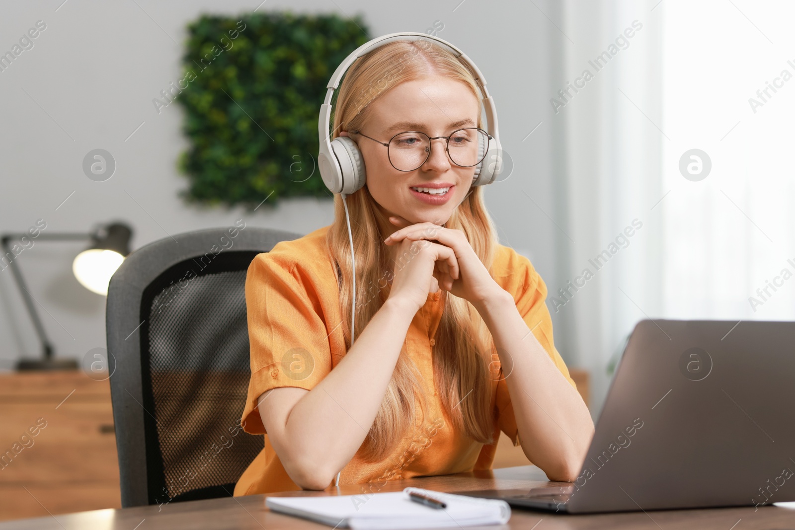 Photo of Interpreter in headphones working with laptop at table indoors