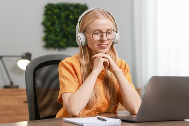 Interpreter in headphones working with laptop at table indoors