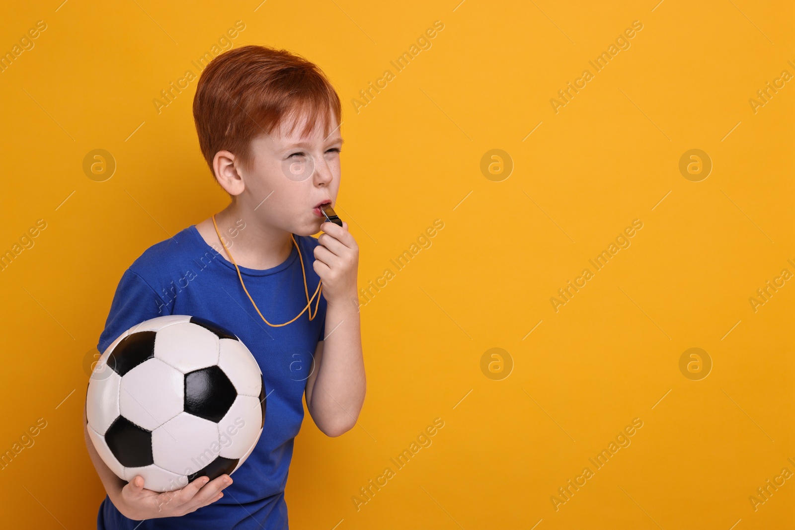 Photo of Little boy with soccer ball blowing whistle on orange background, space for text