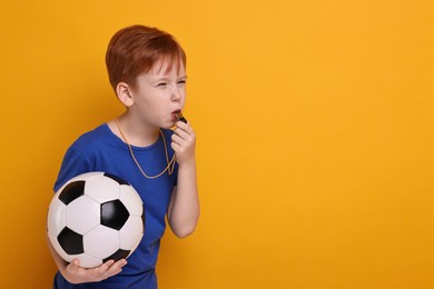 Photo of Little boy with soccer ball blowing whistle on orange background, space for text