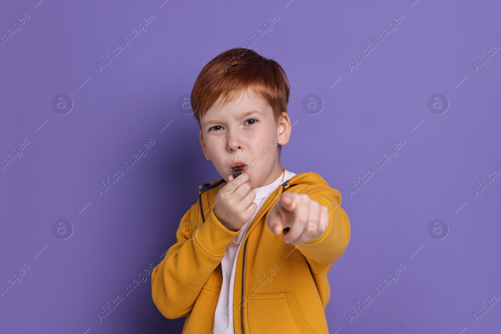 Photo of Little boy blowing whistle on purple background