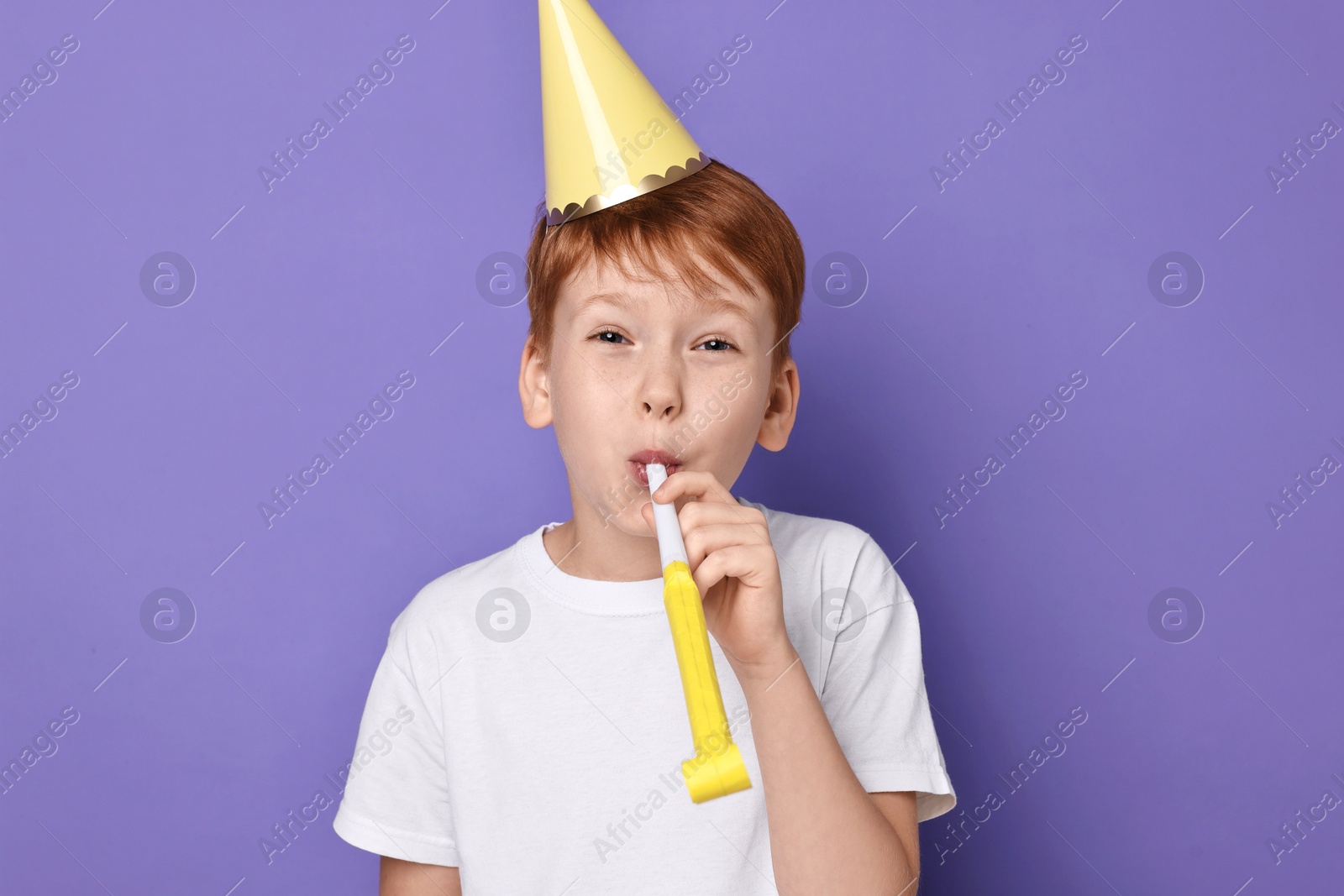 Photo of Little boy in party hat with blower on purple background