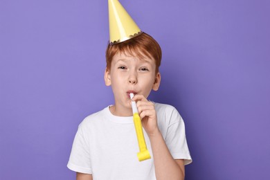 Photo of Little boy in party hat with blower on purple background