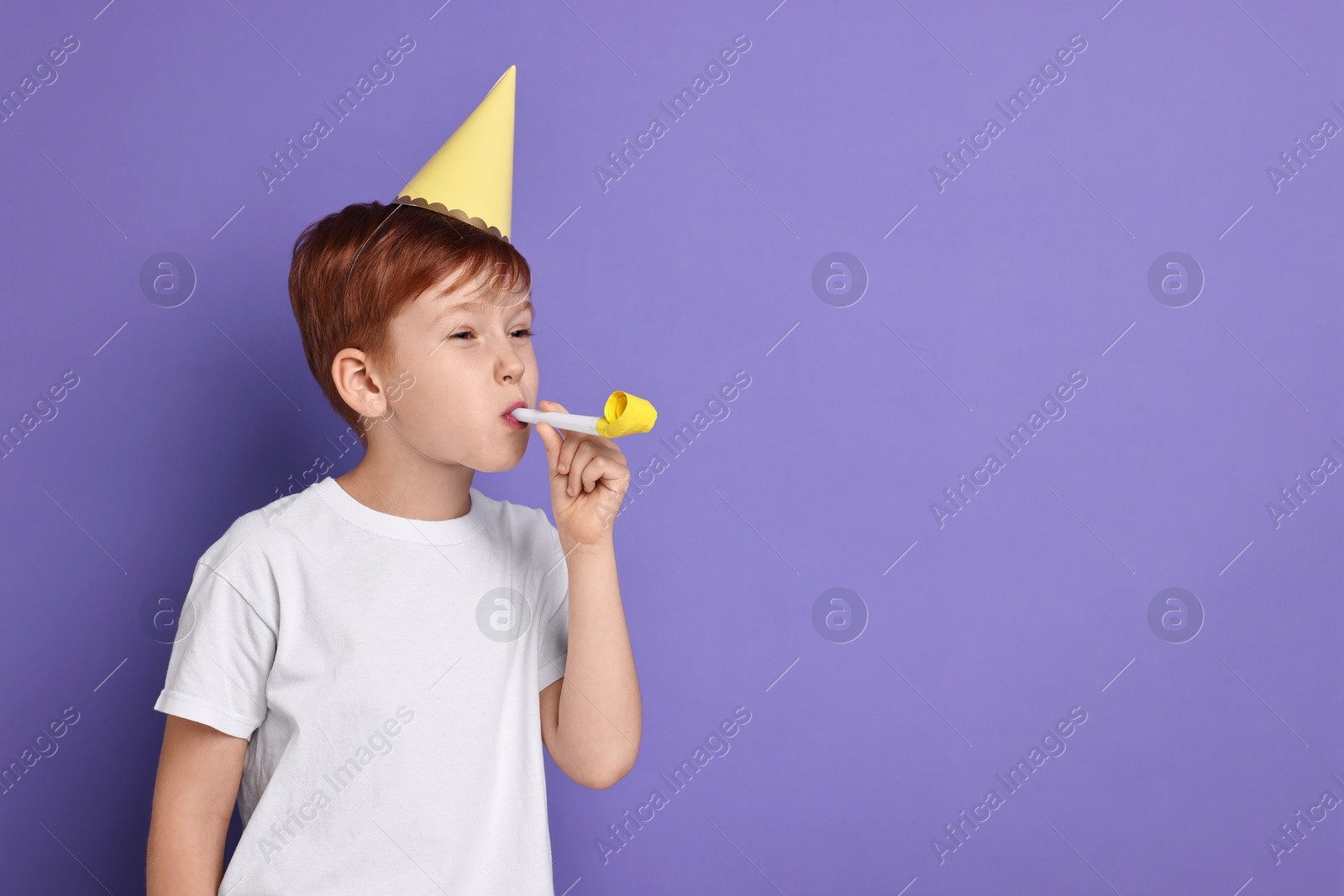 Photo of Little boy in party hat with blower on purple background, space for text